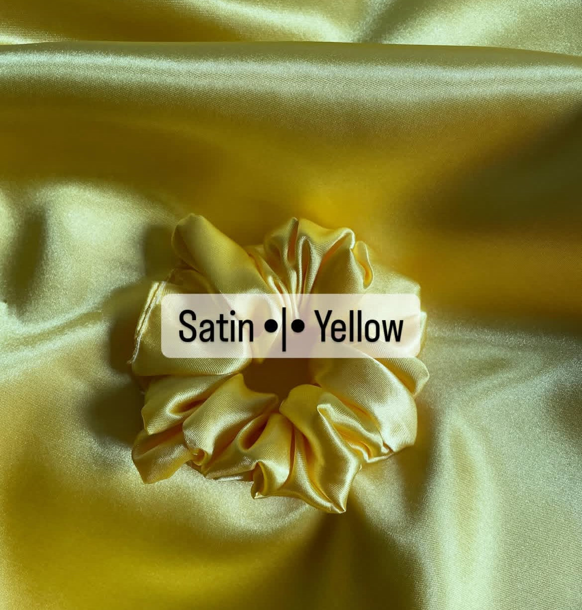 Yellow satin fabric with a scrunchie and text label on a yellow background