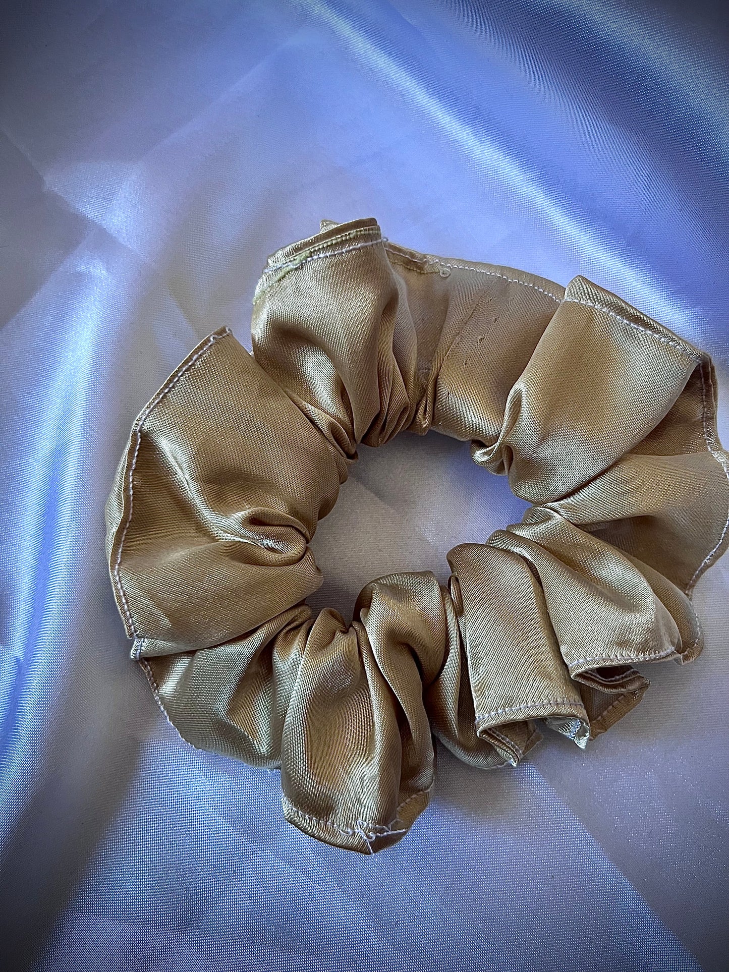 Beige satin scrunchie on a light blue fabric background