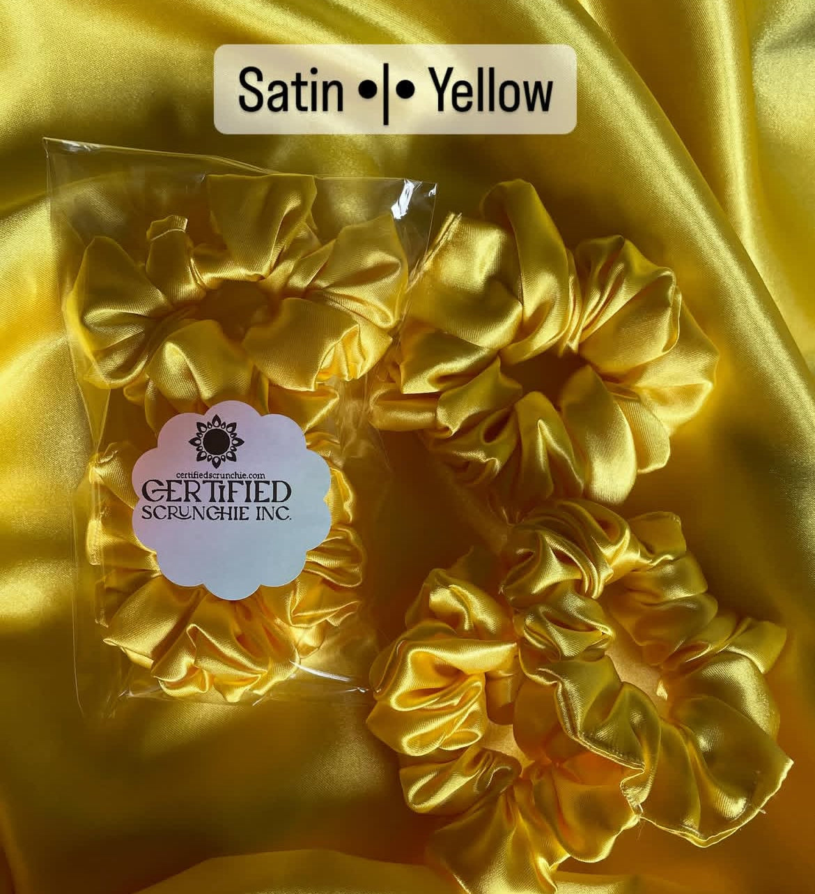 Yellow satin scrunchies with a 'Certified Scrunchie Inc.' label on a yellow satin background.